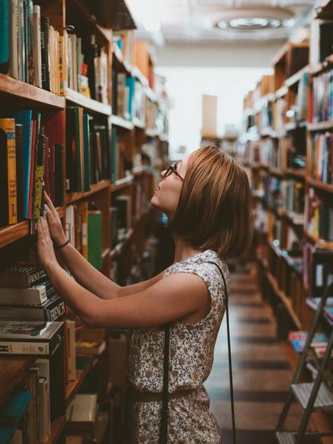 A woman in glasses selects a book from a shelf in a library.