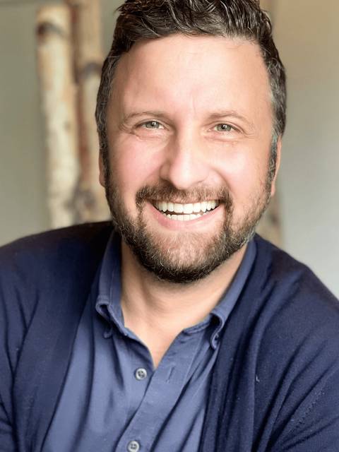 A portrait of a smiling man with a beard wearing a blue shirt.