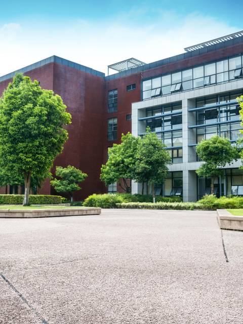 A modern educational building surrounded by lush green trees under a clear sky.