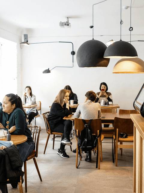 People socializing and working in a modern cafe with bright lighting and minimalist decor.