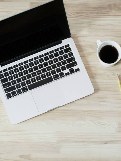 An open laptop with a cup of coffee and notepad on a wooden desk.