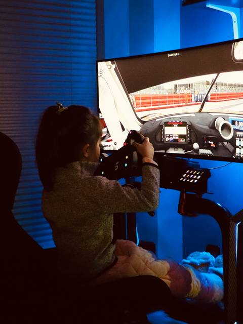 A young girl is using a racing simulator setup in a room with blue lighting.