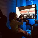 A young girl is using a racing simulator setup in a room with blue lighting.