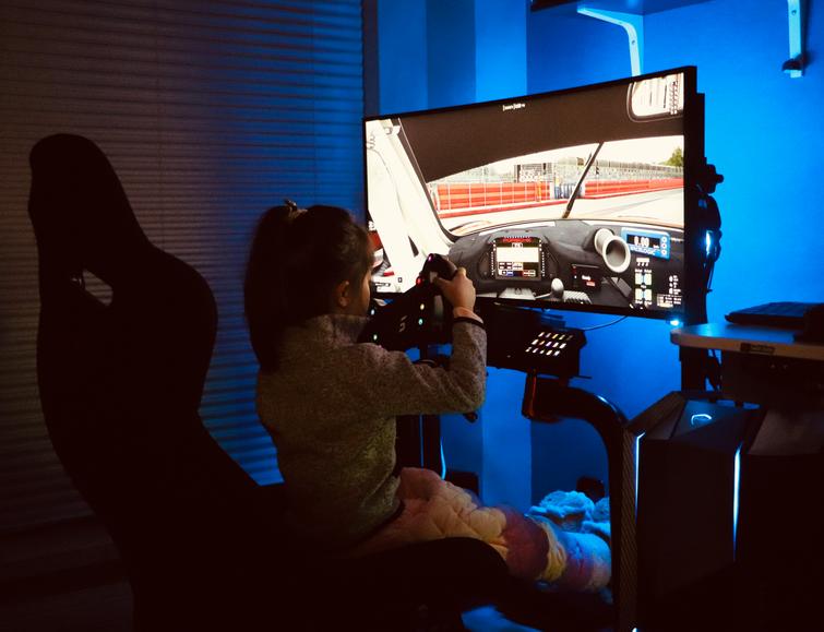 A young girl is using a racing simulator setup in a room with blue lighting.