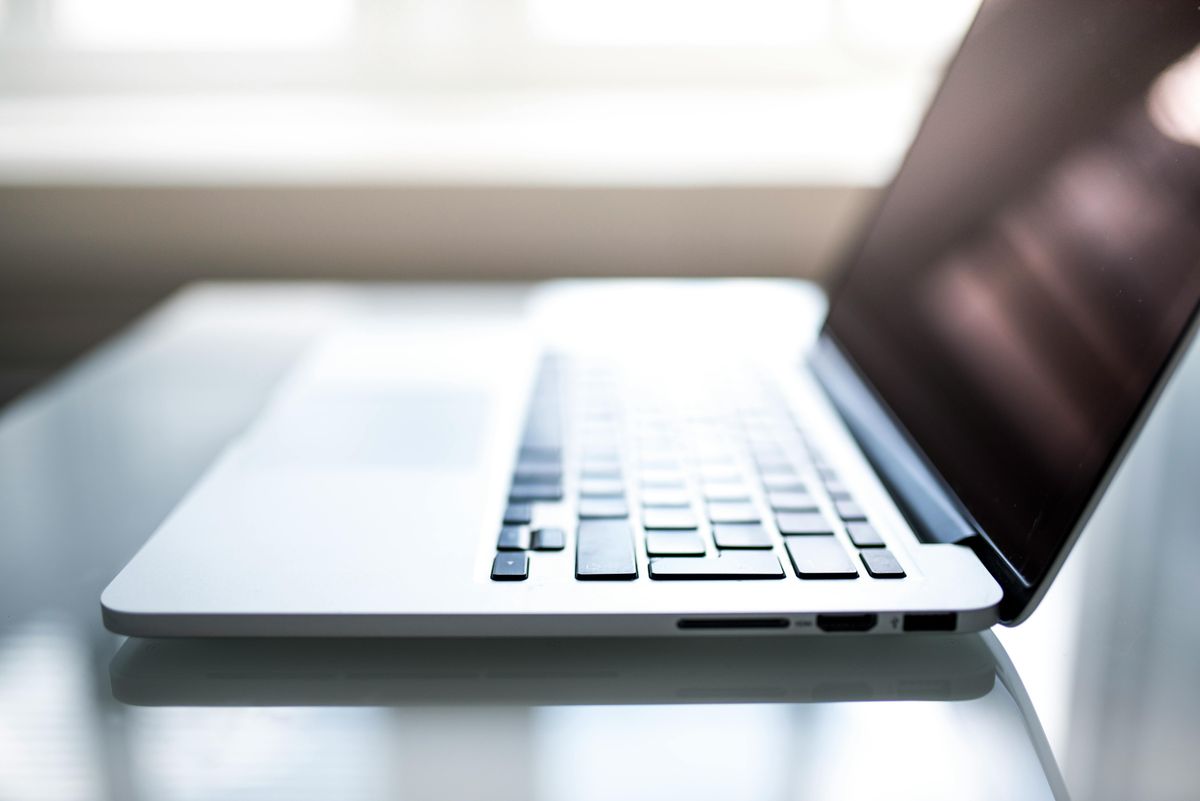 An open laptop on a glass table, illuminated by natural light from a window.