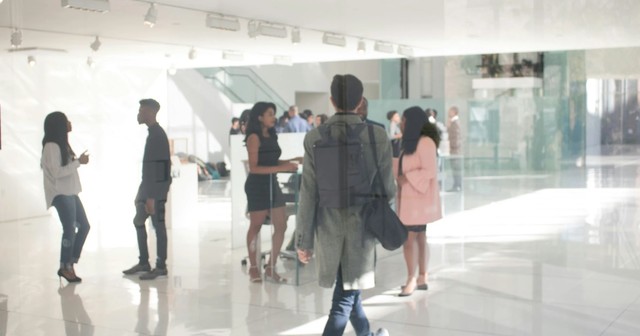 A young man with a backpack walking towards a group of people in a brightly lit modern gallery space.