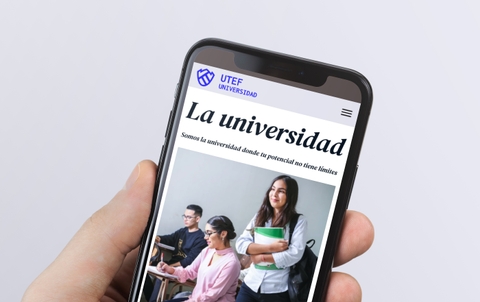 A person holding a smartphone displaying a university's promotional webpage featuring students in a classroom.