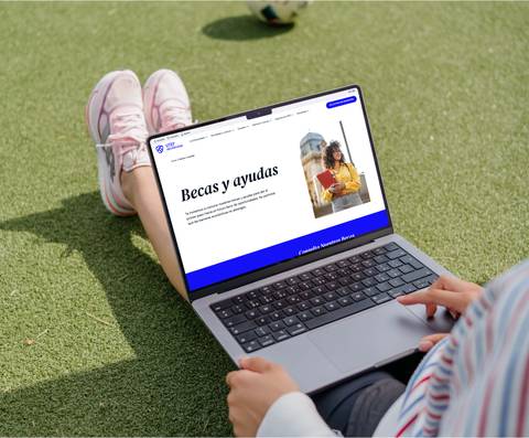 Person using a laptop displaying a webpage about scholarships and aids while sitting on green grass.